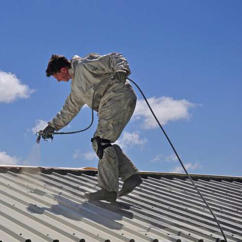 a worker spraying a metal roof coating